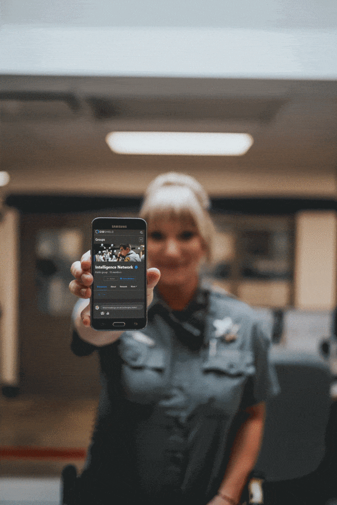 A woman holds a cell phone displaying the police department logo, emphasizing community engagement and communication.